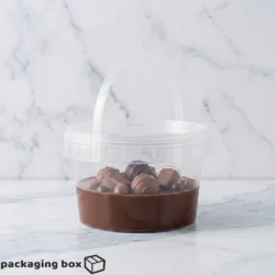 Clear transparent plastic round bucket with snap lid and handle 500gm — food-grade chocolate and sweet packaging in Pakistan.