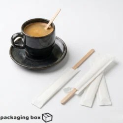 Individually paper-wrapped natural wooden stir sticks for tea and coffee displayed next to a dark ceramic espresso cup with wooden stirrer – by Packaging Box