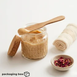 Hygienic wooden wax spatula resting on open glass jar with wax, cork lid and dried rose petals on white background
