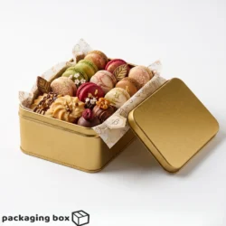Square golden tin box filled with assorted French macarons, cookies and chocolates with decorative tissue paper