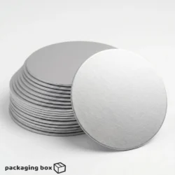 Silver Cake Board under a single-tier ivory buttercream cake with white roses and silver leaf decorations, with stacked silver cake boards visible in background by Packaging Box Pakistan