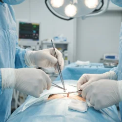 Two surgeons wearing white sterile disposable surgical gloves performing a medical procedure in an operation theatre — available at PackagingBox.pk